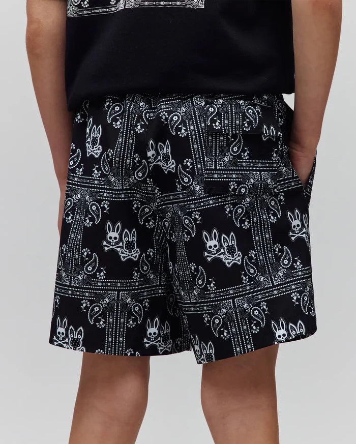 Kids Luke Swim Trunk, black with a vibrant white all-over bandana print, intricately featuring repeated Psycho Bunny skull and crossbones logos, offering a comfortable relaxed fit in a smooth, quick-dry fabric.