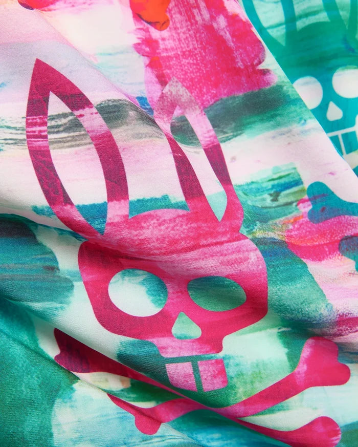Kids Nate All Over Print Swim Trunk with a vibrant abstract watercolor pattern in hot pink, teal, and green, featuring large repeating Psycho Bunny skull and crossbones logos on smooth fabric.