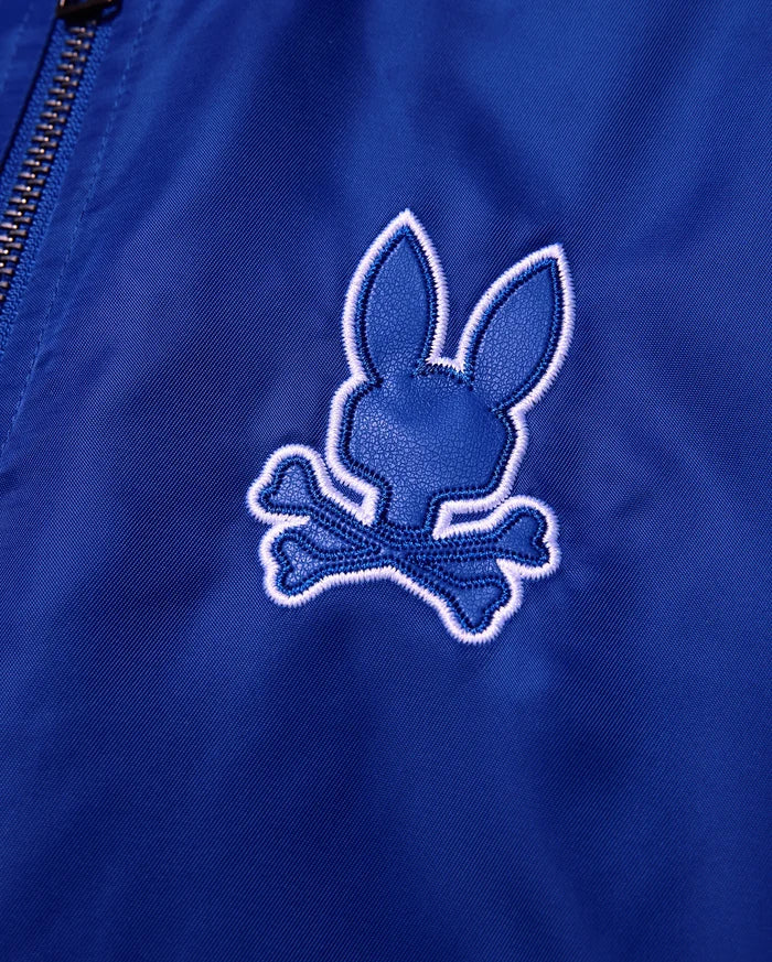 Kids Nathaniel Satin Coach Jacket in smooth royal blue, featuring a prominent textured dark blue Psycho Bunny skull logo with a thick white embroidered outline.