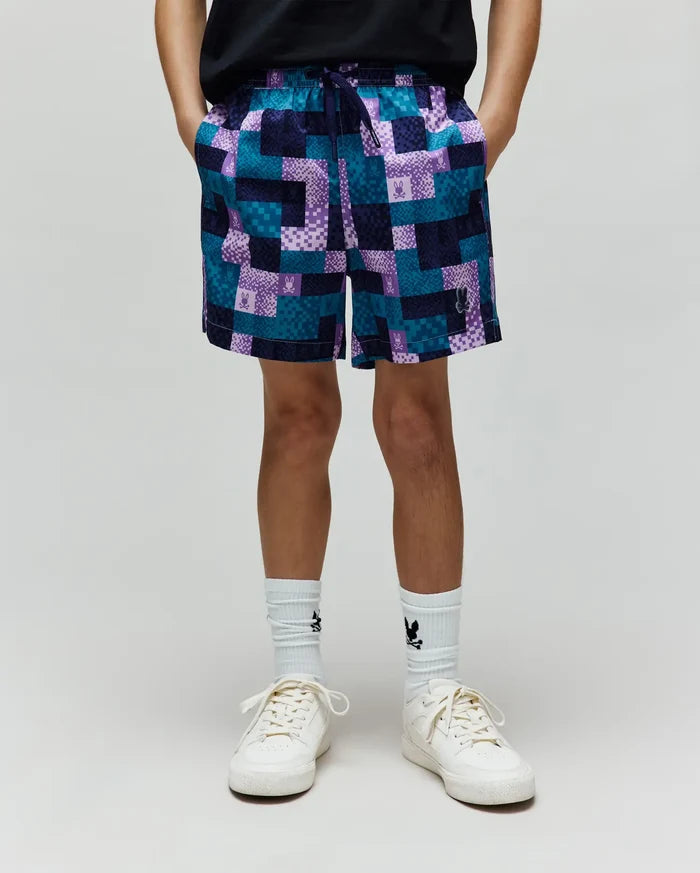 Kids Olivier All Over Bunny Swim Trunk in a relaxed fit, featuring a vibrant teal, purple, and navy patchwork pattern with small integrated Psycho Bunny skull logos throughout. Smooth, quick-dry fabric.