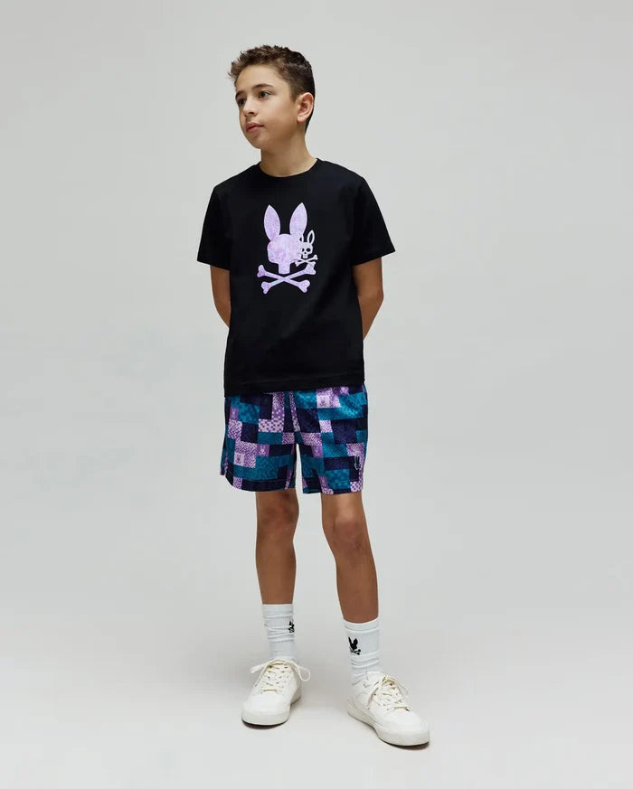 Black classic-fit jersey t-shirt with a large lavender Psycho Bunny skull graphic on the chest, paired with Kids Olivier All Over Bunny Swim Trunk, a blue and purple patchwork short with small bunny logos.