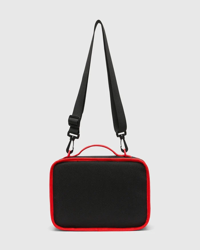 Kids Pal Lunch Box, sleek black durable fabric with vibrant red piping, a sturdy top handle, and an adjustable black shoulder strap featuring red carabiner clips.