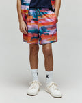 Kids Raphael Swim Trunk, relaxed fit, quick-dry fabric. Features a vibrant abstract print in orange, pink, blue, purple, teal, with a small embroidered Psycho Bunny skull logo on the lower left leg.