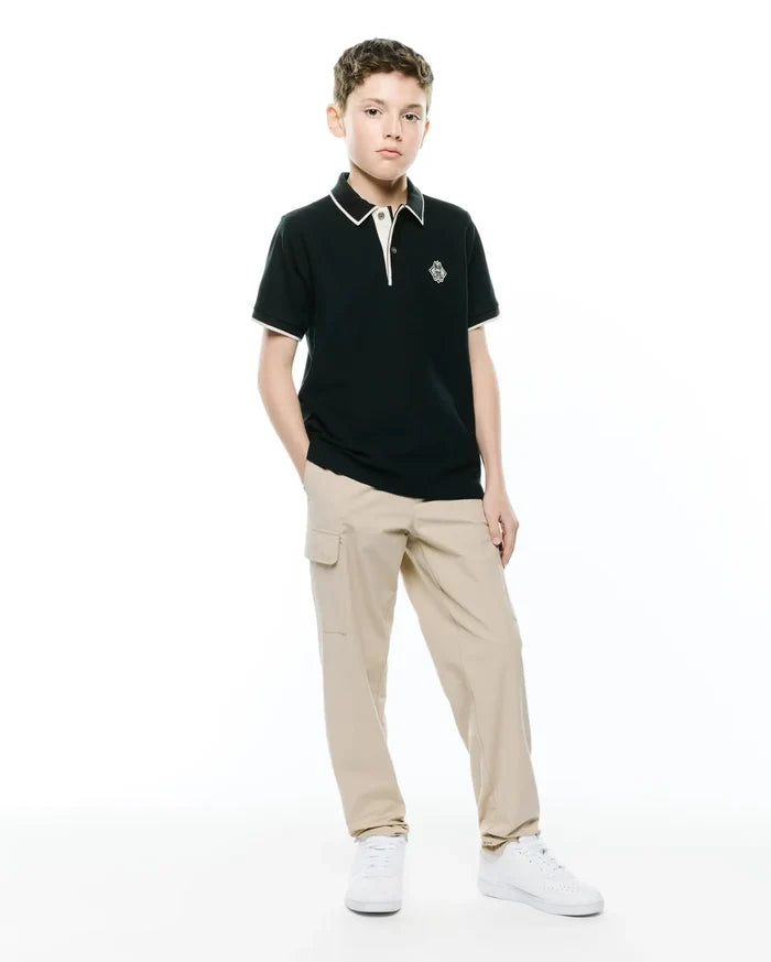 Kids Robin Pique Polo, a classic fit dark green pique polo with white/cream tipping on the collar and cuffs, featuring an embroidered Psycho Bunny skull logo on the left chest.