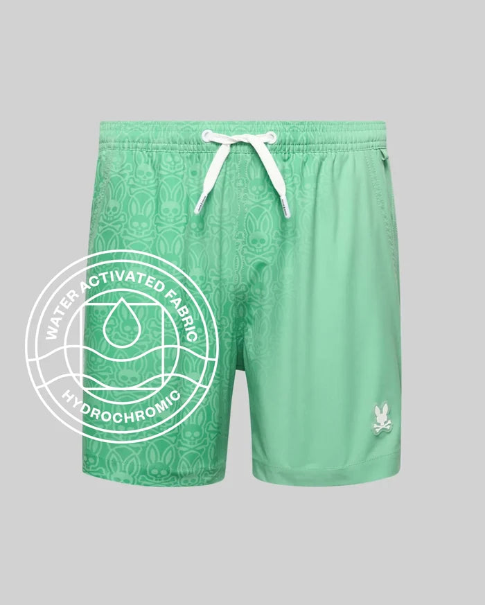 Kids Samos Hydrochromic Printed Swim Trunk in mint green, featuring a relaxed fit, white drawstrings, and a small white Psycho Bunny skull logo on the lower right leg. The smooth fabric reveals a tonal bunny skull pattern when wet.