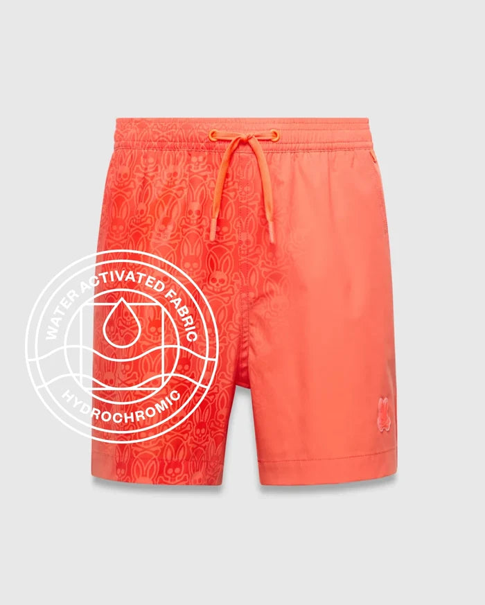 Kids Samos Hydrochromic Printed Swim Trunk in vibrant coral, featuring a water-activated all-over Psycho Bunny skull pattern on the left, solid right leg, and small embroidered bunny logo.