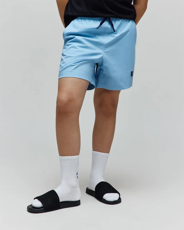 Kids Samos Hydrochromic Printed Swim Trunk in light blue, featuring a relaxed fit, smooth quick-dry fabric, navy drawstring, and a small embroidered Psycho Bunny skull logo on the lower left leg.