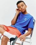 Kids Sunny Chest Graphic Tee, a royal blue jersey tee with a small embroidered Psycho Bunny skull logo wearing sunglasses on the left chest, paired with coral relaxed fit shorts featuring a subtle embroidered bunny.