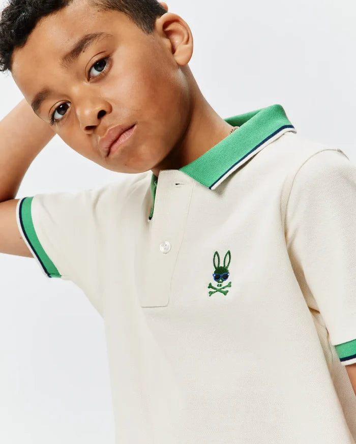 Kids Sunny Pique Polo in cream, featuring a classic fit, green ribbed collar with navy stripe, matching striped cuffs, and a small embroidered green Psycho Bunny skull with blue sunglasses on the left chest.