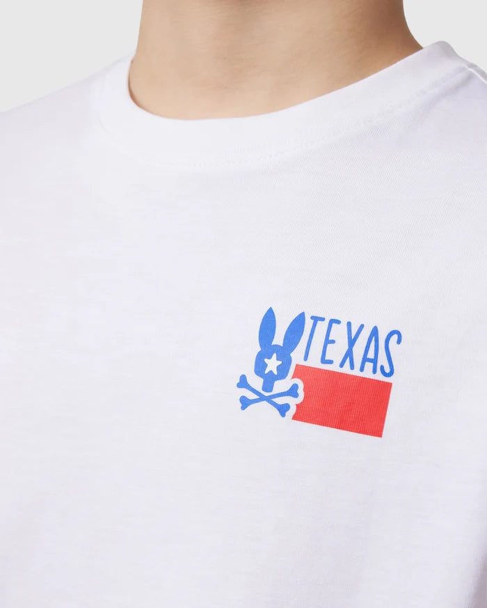 Close-up of a person wearing the Psycho Bunny KIDS TEXAS CITY TEE in white, made from luxurious Peruvian Pima cotton. The vibrant graphic design features a stylized rabbit with bone-like ears and "TEXAS" above a red rectangle displaying the Texas flag pattern.