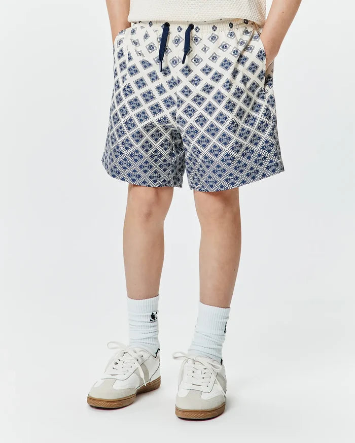 Kids Tobias Swim Trunk, cream with a navy blue all-over geometric pattern of the iconic Psycho Bunny skull logo, relaxed fit, smooth quick-dry fabric, and a navy drawstring.
