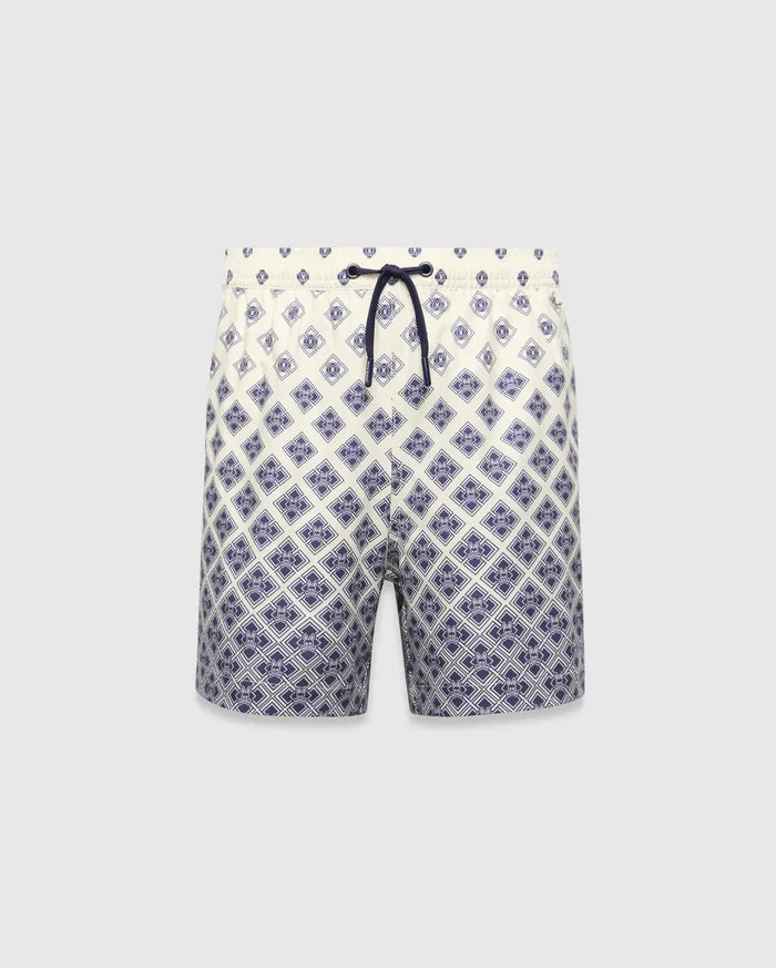 Kids Tobias Swim Trunk in cream with a navy blue diamond grid pattern featuring repeated Psycho Bunny skull logos, a relaxed fit, and a navy drawstring. The pattern intensifies towards the hem.