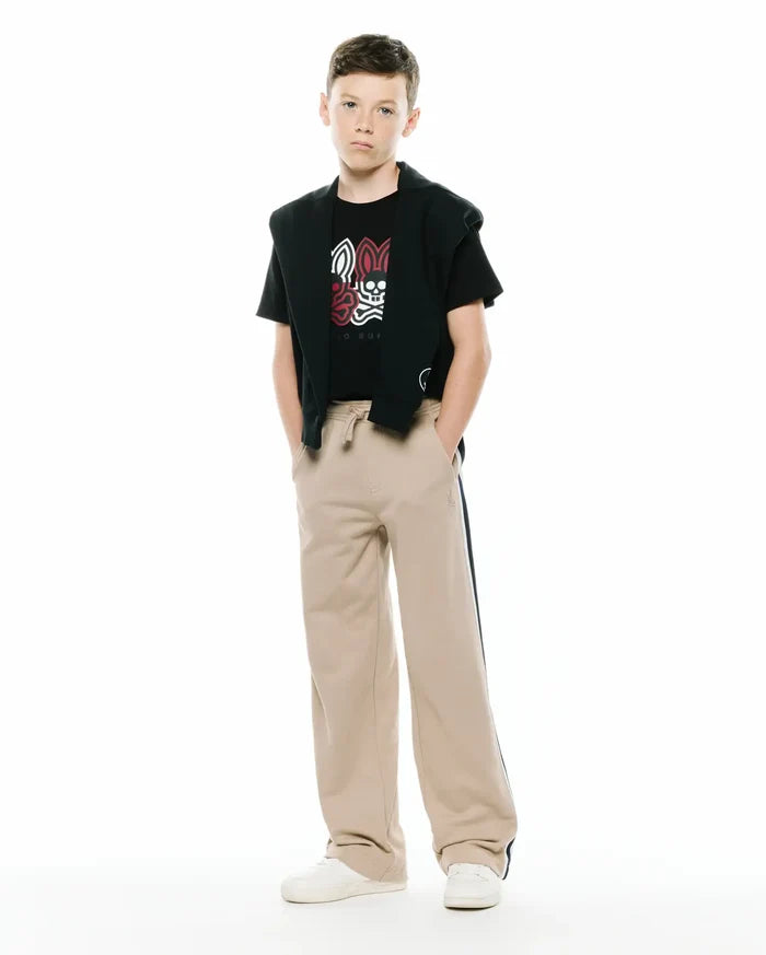 Black jersey t-shirt with a large white and red Psycho Bunny skull graphic, paired with a black French terry hoodie draped over shoulders and KIDS TY FRENCH TERRY SWEATPANT in beige with a dark side stripe and small embroidered logo.