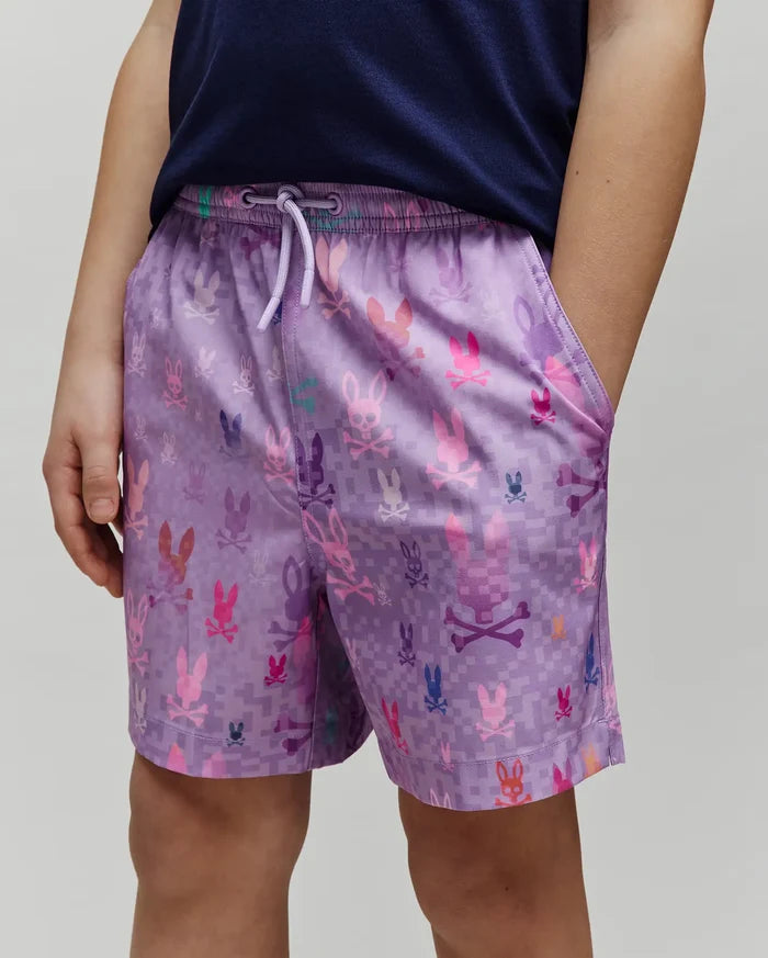Kids Van Swim Trunk in purple, featuring a relaxed fit and an all-over pixelated print of multi-colored Psycho Bunny skull logos in pink, blue, orange, and green on smooth, quick-dry fabric with a drawstring waist.