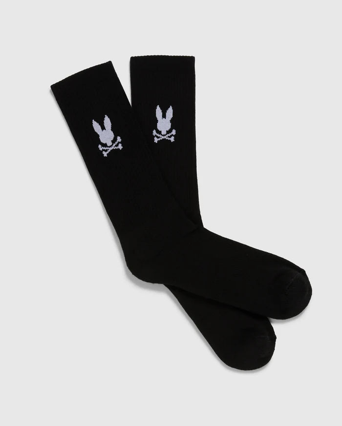 A pack of 3 pairs of black men's knee-high sport socks from the Psycho Bunny brand, featuring a white skull and crossbones symbol with bunny ears on each sock. Made from luxurious Peruvian pima cotton, these MENS 3 PACK SPORT SOCK - B6F997D200 socks are displayed positioned overlapping each other against a plain, light gray background.