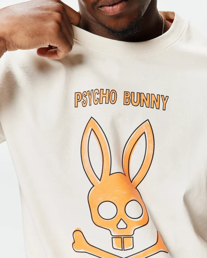 Mens Adler Graphic Tee, a cream classic fit jersey t-shirt featuring a large orange and black Psycho Bunny skull graphic and PSYCHO BUNNY text on the chest.