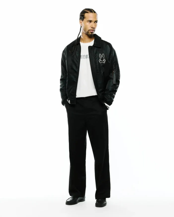 Black satin-like bomber jacket with a large white Psycho Bunny skull logo, a white jersey t-shirt with black Psycho Bunny text, and relaxed fit Black Mens Aidan Chino Pant.