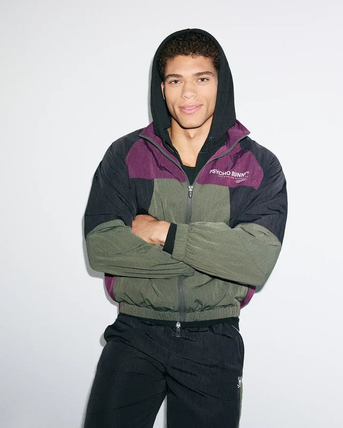 Mens Alder Nylon Colorblock Jacket, a relaxed fit, full-zip hooded jacket in crinkled nylon. Features black, deep purple, and olive green panels with a white Psycho Bunny chest logo and bunny skull zipper pull.