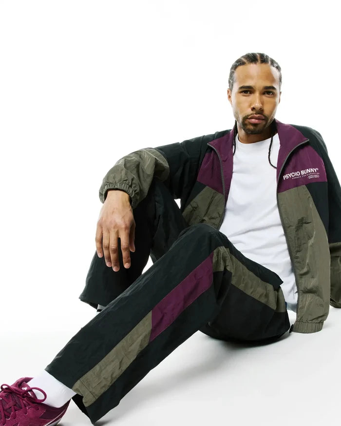 Mens Alder Nylon Colorblock Pant and matching relaxed-fit full-zip track jacket in black, olive green, and deep purple crinkled nylon, with a white Psycho Bunny chest logo.