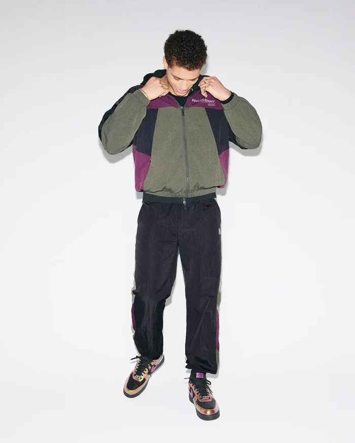 Olive, black, and purple colorblock crinkled nylon windbreaker jacket with Psycho Bunny chest text logo, paired with matching Mens Alder Nylon Colorblock Pant featuring side stripes and an embroidered bunny skull.