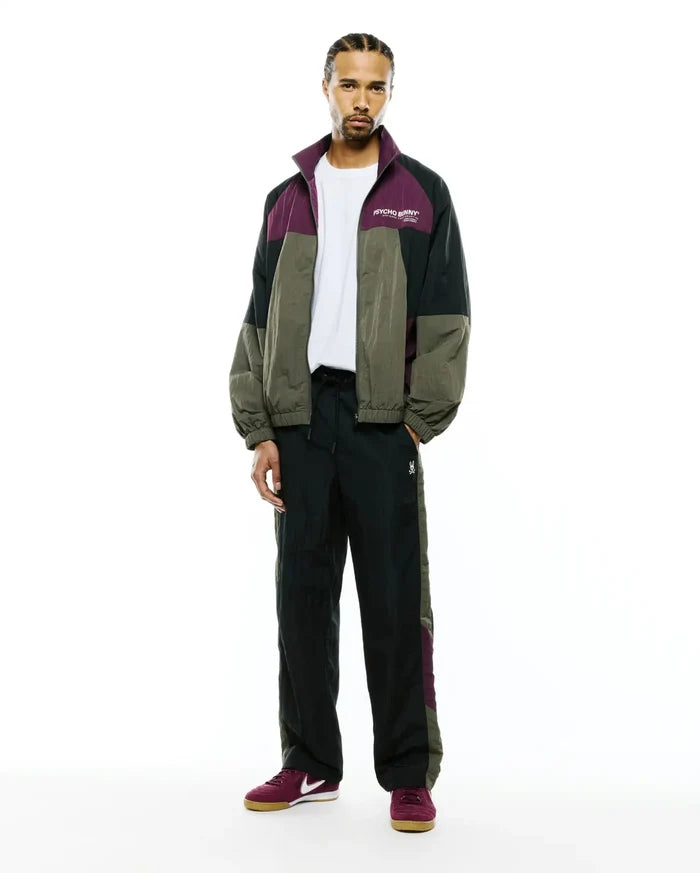 Relaxed crinkled nylon colorblock jacket in green, black, and purple with a white chest Psycho Bunny logo, matching Mens Alder Nylon Colorblock Pant with side panels and a small bunny skull.