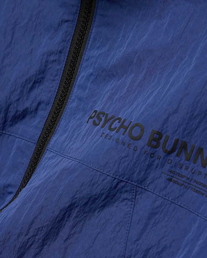 Mens Alder Nylon Jacket in navy blue with crinkled texture, featuring a black full-zip and large black Psycho Bunny text print with Designed For Disrupt slogan and coordinates.