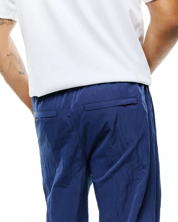 MENS ALDER NYLON PANT in deep navy blue, showcasing a distinctive crinkled nylon fabric texture, a comfortable relaxed fit, and practical rear flap pockets.