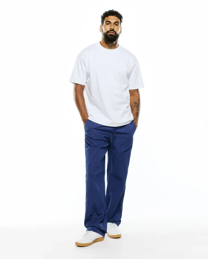 Relaxed fit white jersey t-shirt paired with MENS ALDER NYLON PANT in deep blue, featuring a crinkled texture, drawstring waist, and a comfortable, refined streetwear aesthetic.
