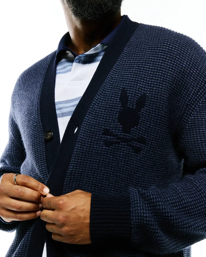 Mens Atkinson Cardigan, a relaxed fit navy blue waffle knit cardigan with ribbed cuffs and hem, featuring a large tonal embroidered Psycho Bunny skull logo on the left chest and a single visible button closure.