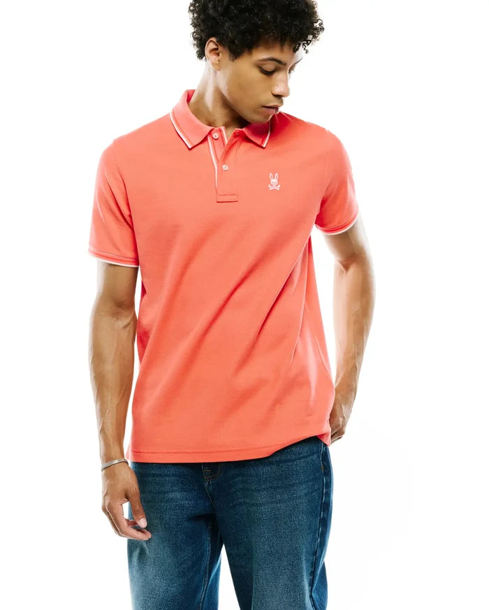 Mens Atley Pique Polo in vibrant coral, featuring a classic fit, textured pique fabric, white tipping on the collar and cuffs, and a small embroidered Psycho Bunny skull logo on the left chest.
