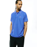 Mens Atley Pique Polo in vibrant royal blue, featuring a classic fit, pique knit fabric, white tipped collar and cuffs, and a small embroidered magenta Psycho Bunny skull logo on the left chest.