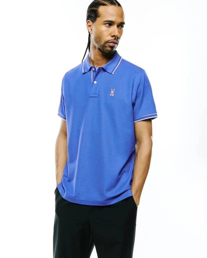 Mens Atley Pique Polo in vibrant royal blue, featuring a classic fit, pique knit fabric, white tipped collar and cuffs, and a small embroidered magenta Psycho Bunny skull logo on the left chest.