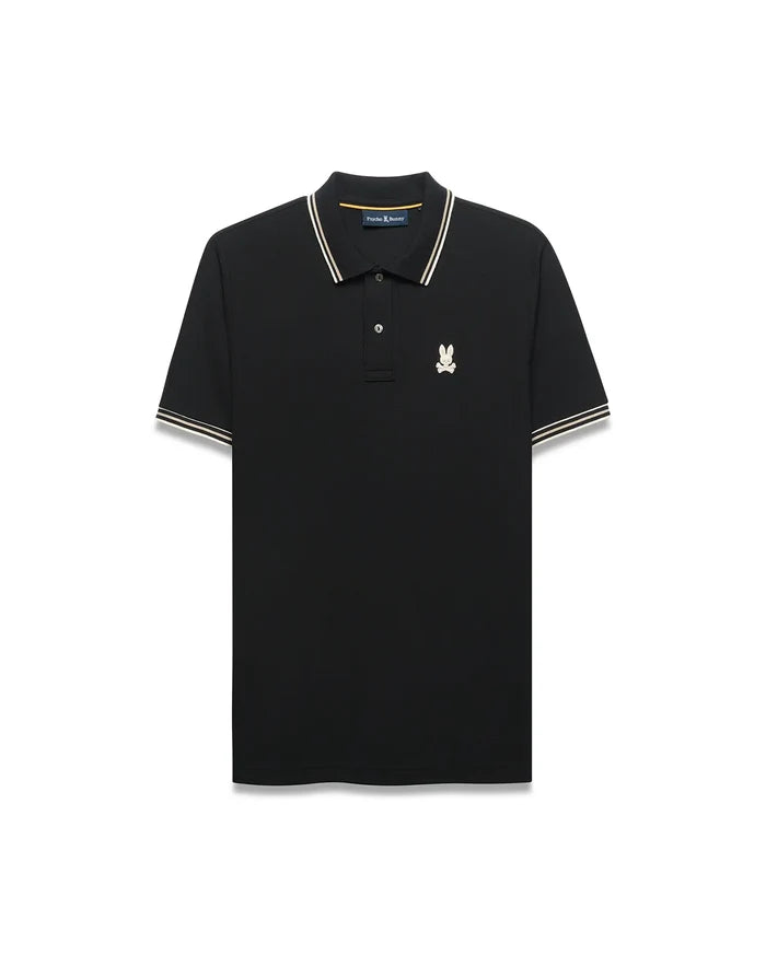 Mens Atley Pique Polo in black, featuring a classic fit, pique texture, white and gold striped collar and sleeve cuffs, and a small embroidered cream and gold Psycho Bunny skull logo on the left chest.