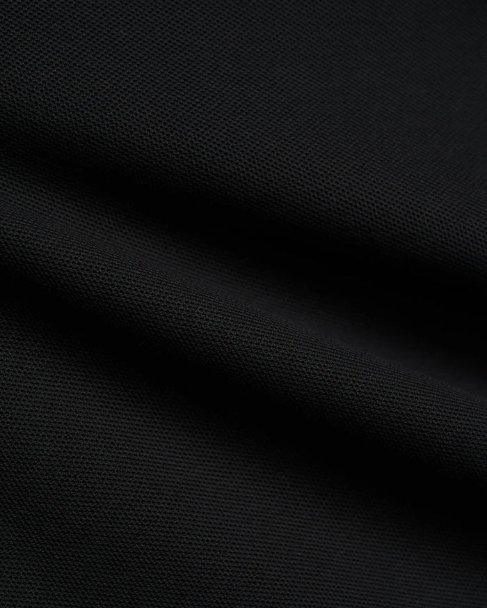 Psycho Bunny Mens Atley Pique Polo in deep black, showcasing the premium, breathable textured pique fabric with subtle folds, perfect for sophisticated streetwear.