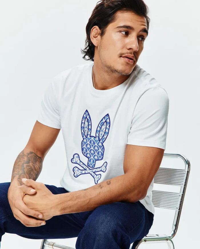 Mens Brad Graphic Tee, a crisp white classic fit jersey t-shirt showcasing a prominent blue and white intricate patterned Psycho Bunny skull logo graphic on the chest.