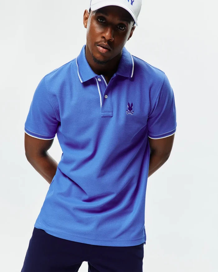 Mens Brad Pique Polo in royal blue, featuring a classic fit, pique knit fabric, white tipped collar and cuffs, and a small embroidered purple Psycho Bunny skull logo on the left chest.