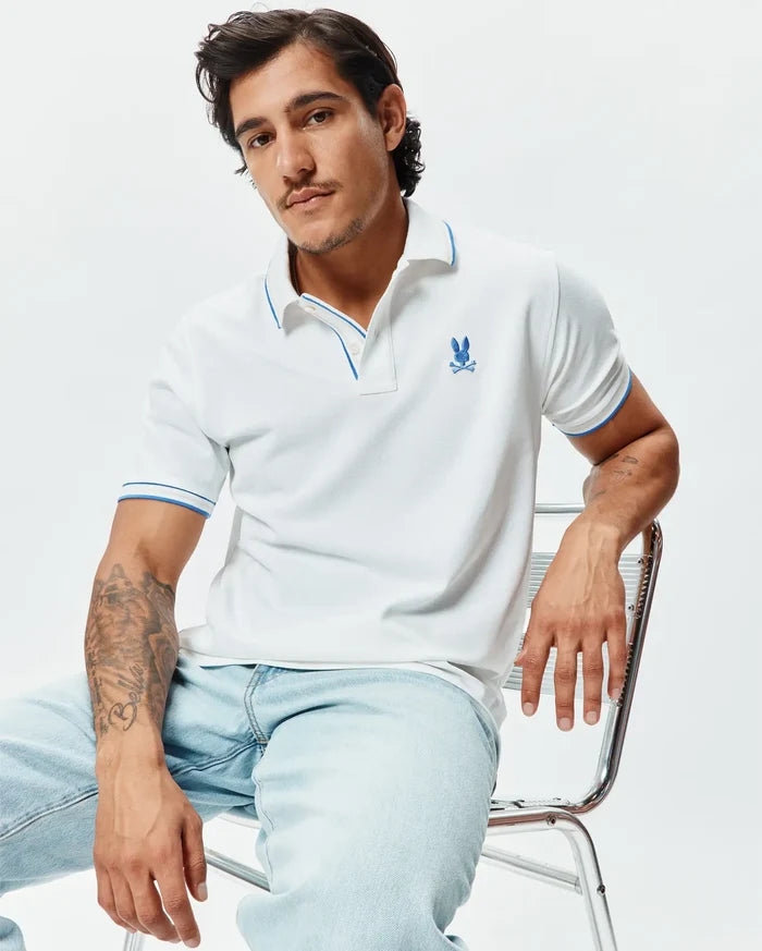 Mens Brad Pique Polo, white pique knit with blue trim on collar and sleeve cuffs, featuring an embroidered blue Psycho Bunny skull logo on the left chest, classic fit.