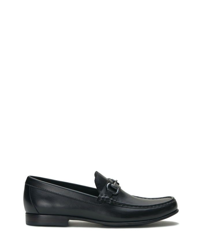 The Vince Camuto Men’s Caelan Loafer is a black leather slip-on with a low heel and buckle detail, displayed in side profile against a white background—these classic loafers are an ideal choice for stylish office footwear.