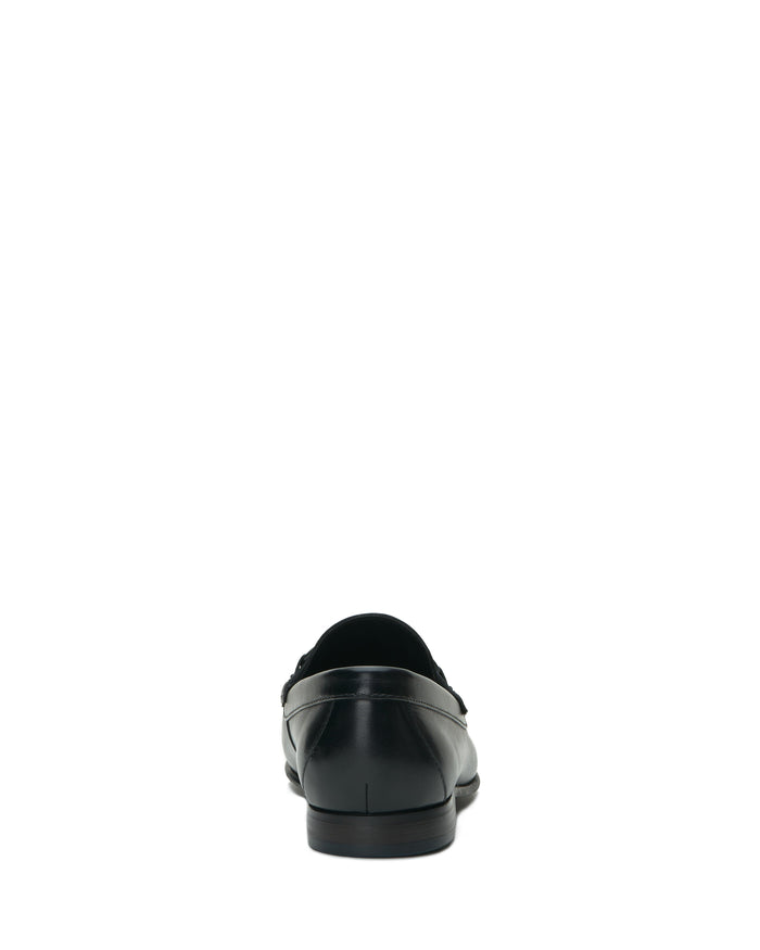 The Vince Camuto Men’s Caelan Loafer, a single black leather shoe featuring classic horse-bit hardware, is shown from the back and centered on a plain white background.