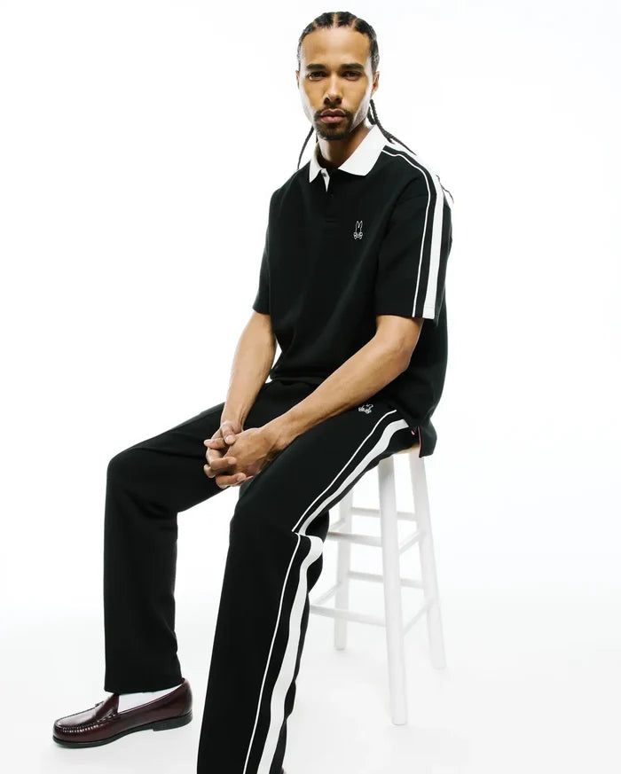 Black pique polo, classic fit, with white collar, sleeve stripes, and embroidered Psycho Bunny skull logo, plus Mens Ceano Track Pant with white side stripes and a thigh logo.