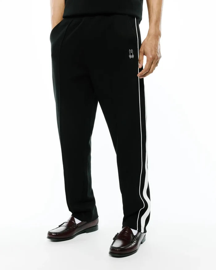 Black Mens Ceano Track Pant, relaxed fit, smooth knit, with a distinctive white wavy side stripe and a small embroidered white Psycho Bunny skull logo on the left hip.