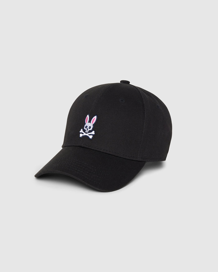 A Psycho Bunny MENS CLASSIC BASEBALL CAP - B6A816A1HT in black featuring a small embroidered pink and white bunny above crossed bones on the front. Made from durable cotton twill, it has a curved brim and six panels with eyelets for ventilation. The background is plain and light gray.