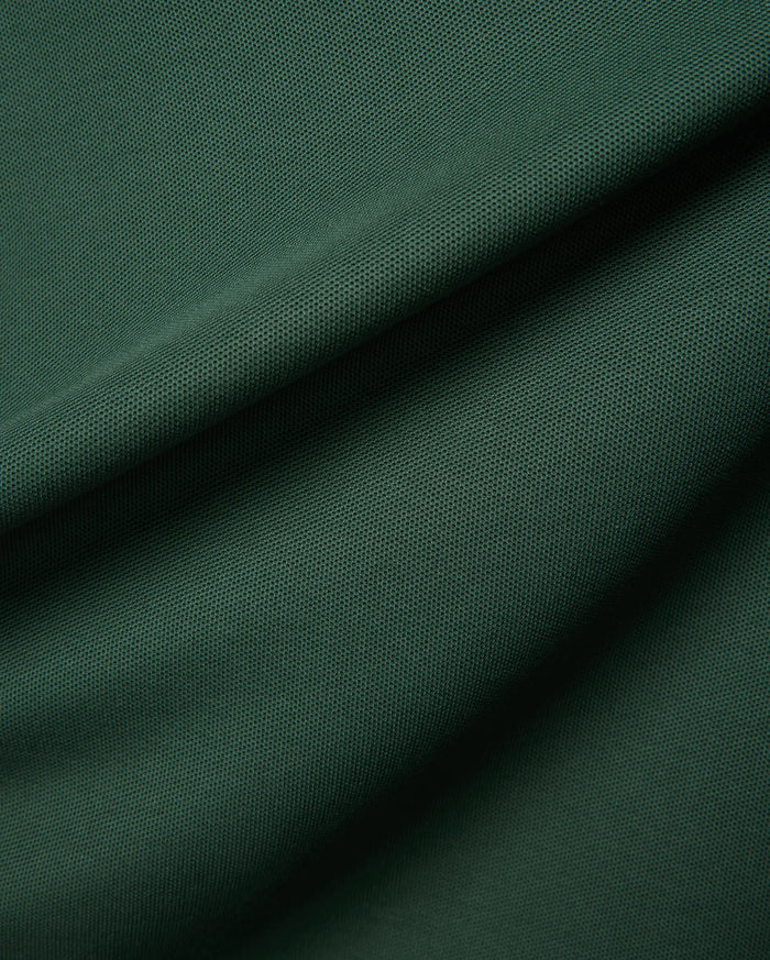 Mens Classic Pique Polo in a deep forest green, highlighting the refined, textured pique fabric with elegant folds, embodying Psycho Bunny's premium streetwear.