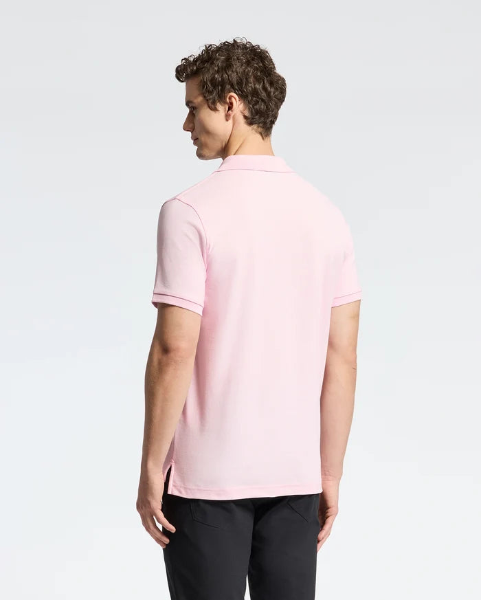 A man in a Psycho Bunny MENS CLASSIC PIQUE POLO SHIRT - B6K001CRPC, light pink, pairs it with black pants. He stands back facing the camera on a plain white background.
