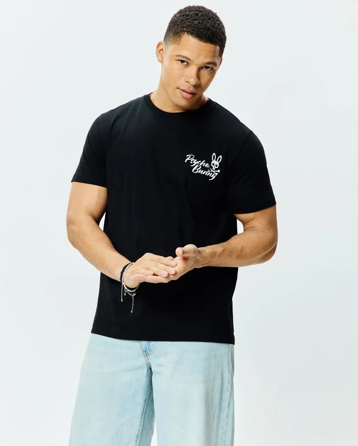 Mens Colin Back Graphic Tee, a black classic fit jersey t-shirt with a prominent white embroidered Psycho Bunny skull and crossbones logo and script text on the left chest.