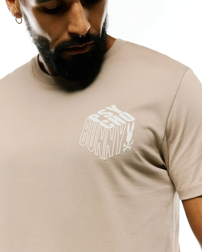 Mens Conan Back Graphic Tee, a classic fit light beige jersey t-shirt with a prominent white 3D block Psycho Bunny text graphic and skull logo on the chest.