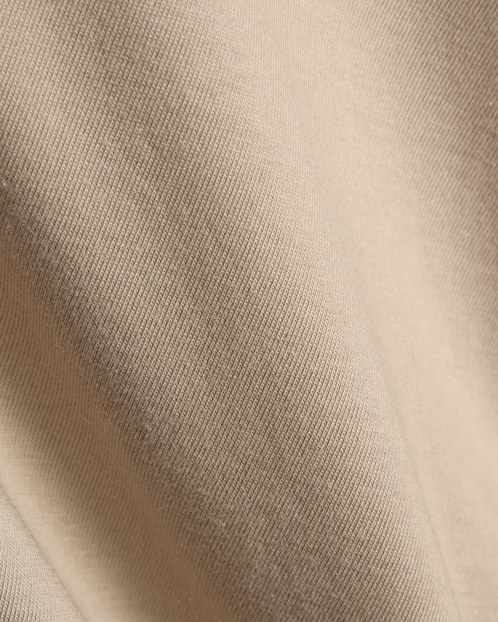 Psycho Bunny Mens Conan Back Graphic Tee in a warm, light beige, showcasing the refined, soft diagonal ribbed knit jersey fabric texture, characteristic of premium streetwear.