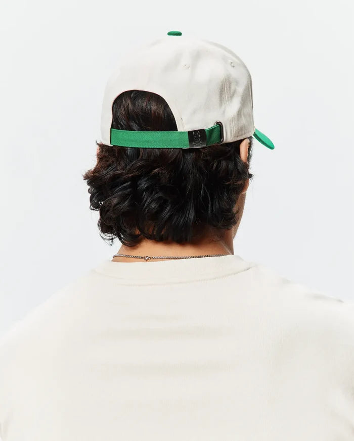 Mens Craig Baseball Cap in cream cotton twill with a green brim and adjustable strap featuring a small Psycho Bunny skull logo on the metal buckle.