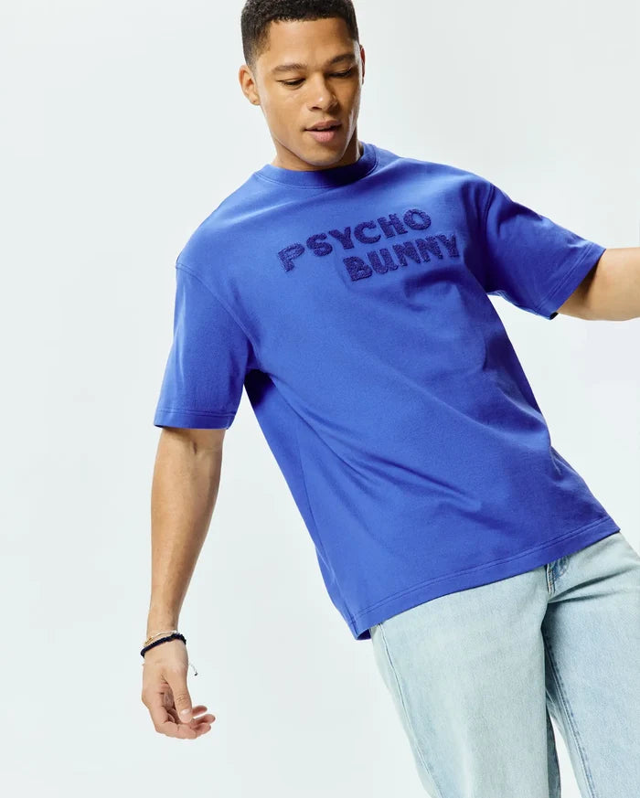 Mens Craig Wordmark Tee, a vibrant royal blue relaxed fit jersey t-shirt featuring a large, tonal embossed PSYCHO BUNNY wordmark across the chest.