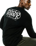 Black Mens Dariel Long Sleeve Back Graphic Tee in soft jersey knit, featuring a large white Psycho Bunny oval graphic on the back with Made In New York Since 2005 text and the iconic bunny skull logo.